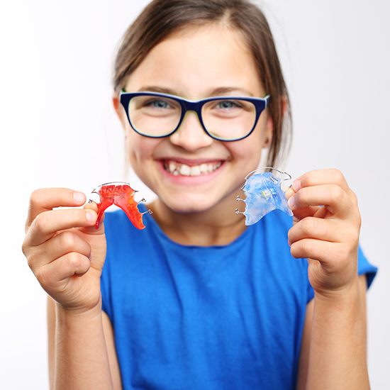 young girl smiling and holding two orthodontic appliances