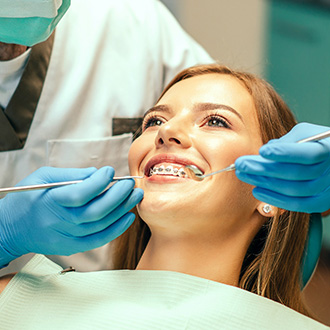 Young woman with braces smiling while orthodontist looks at her teeth