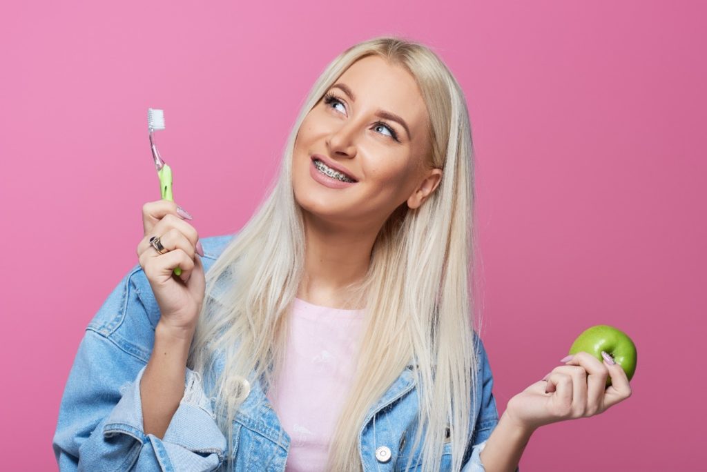 Woman with braces holding toothbrush and an apple