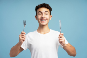 a child with braces smiling and holding a fork